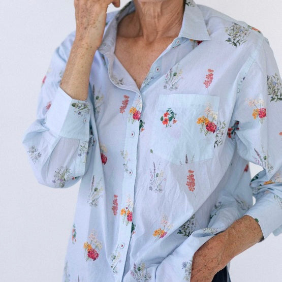 Pale blue button down shirt with small botanical prints all over it in various shades of red, pink, cream and green
