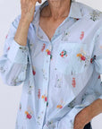 Pale blue button down shirt with small botanical prints all over it in various shades of red, pink, cream and green