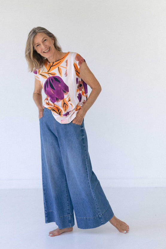 A woman smiles at the camera wearing blue denim wide leg jeans and a colourful top.