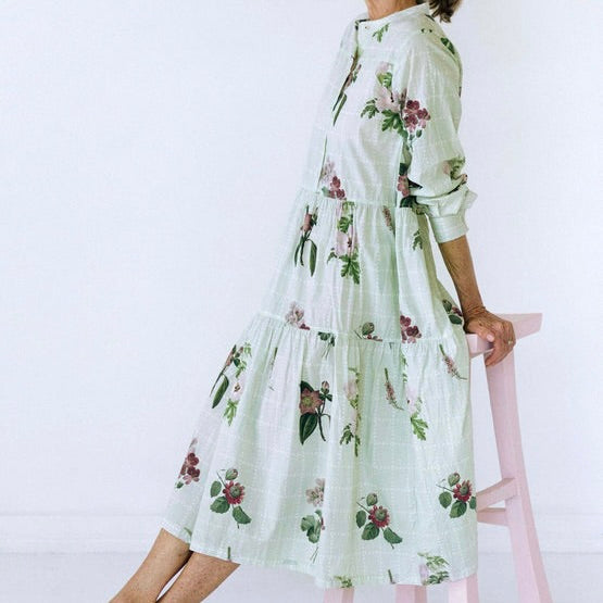 Midi button bodice dress with tiered skirt and botanical print on pale green background.